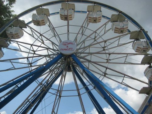 A colorful Ferris wheel against a blue sky with fluffy clouds, showcasing its cabins and structure.
