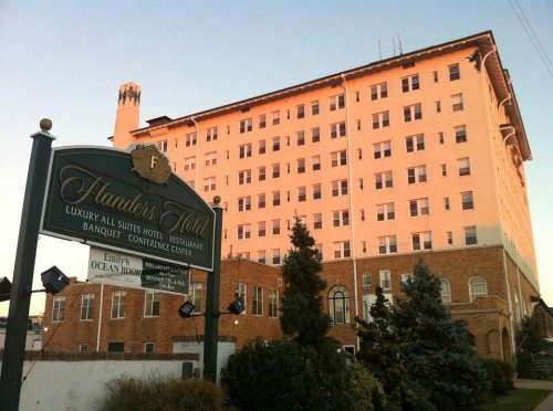 A large pink hotel building with a sign for Flanders Hotel and nearby greenery.