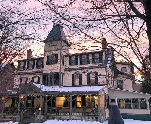 A large, historic house with a tower, surrounded by snow and trees, under a colorful sunset sky.
