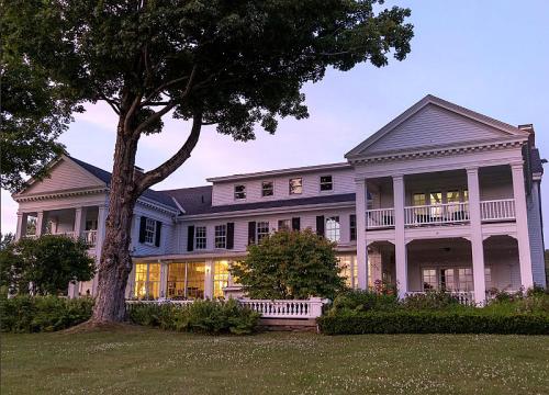 A large, elegant white house with multiple balconies, surrounded by greenery, illuminated at dusk.