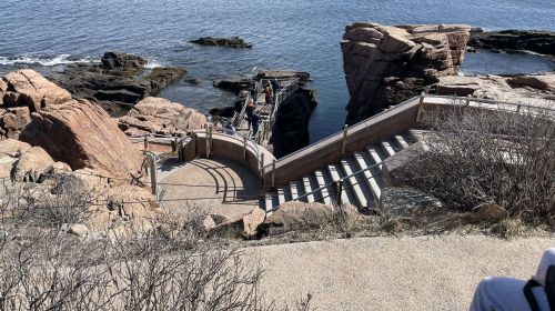 A winding staircase leads down to rocky shores by the water, surrounded by sparse vegetation and coastal scenery.