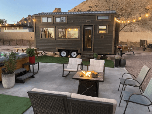 A cozy outdoor seating area with a fire pit, surrounded by a tiny house and mountains in the background.