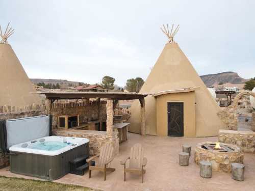 A cozy outdoor area featuring two teepee structures, a hot tub, and a stone fire pit surrounded by chairs.