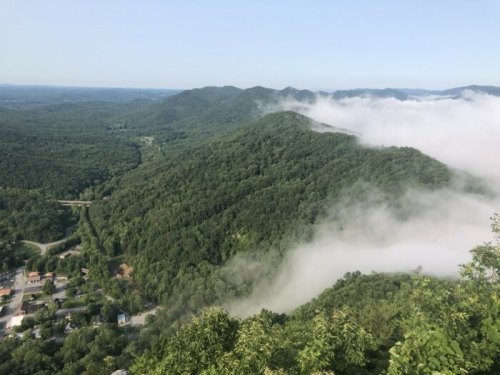 A panoramic view of lush green mountains with fog rolling through the valleys under a clear blue sky.