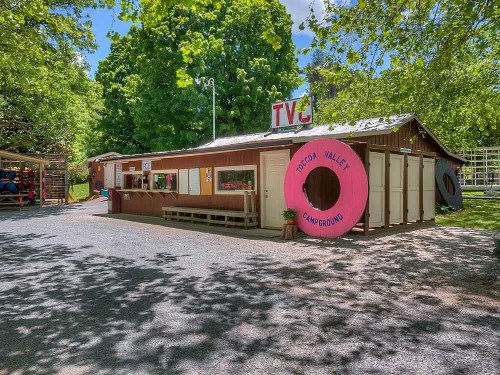 A rustic campground office with a large pink sign, surrounded by trees and gravel pathways.
