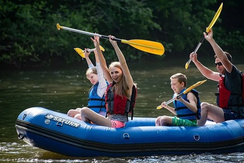 A group of four people in a blue raft, paddling joyfully on a river, surrounded by lush greenery.