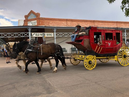 A red stagecoach pulled by two horses travels down a street lined with historic buildings.
