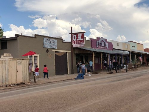Historic buildings line a dusty street, featuring the O.K. Corral and a few visitors enjoying the scenery.