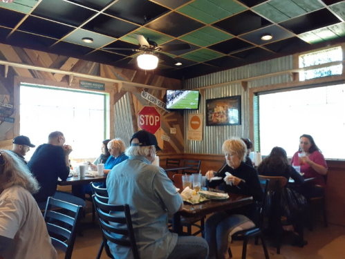 A cozy restaurant interior with patrons enjoying meals, vintage signs on the walls, and a TV showing a sports game.