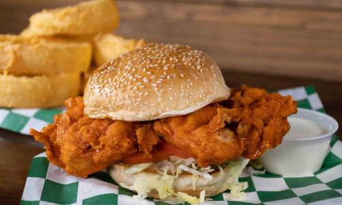A crispy fried chicken sandwich with lettuce and tomato on a sesame seed bun, served with a side of fries.