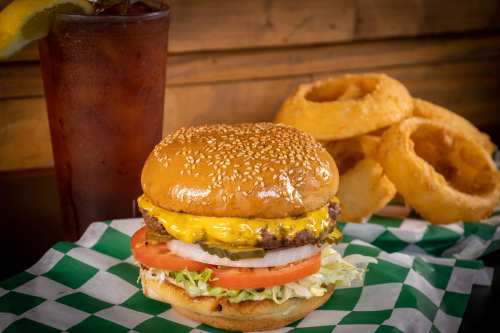 A juicy cheeseburger with lettuce, tomato, and pickles, served with onion rings and a glass of iced tea.