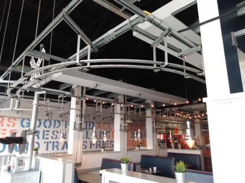 Interior of a modern restaurant featuring industrial decor, overhead tracks, and a vibrant wall with text.