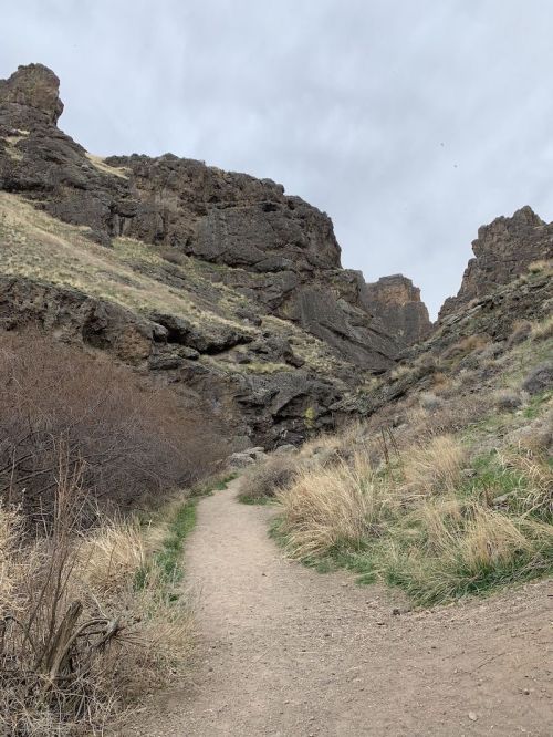 A dirt path winds through rocky terrain and sparse grass under a cloudy sky.