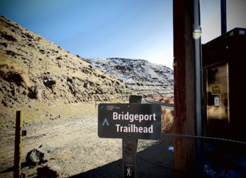 Sign for Bridgeport Trailhead with a mountainous landscape in the background. Clear blue sky above.