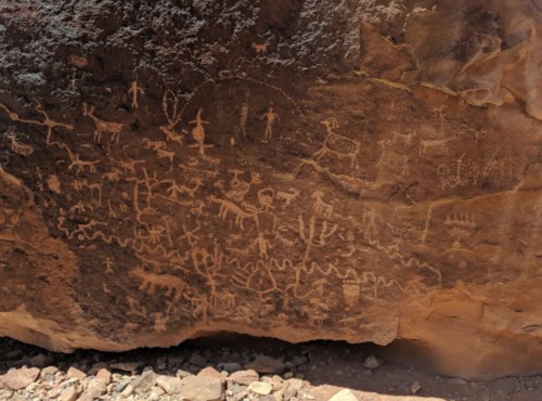 Ancient rock art featuring various figures and animals carved into a large stone surface.