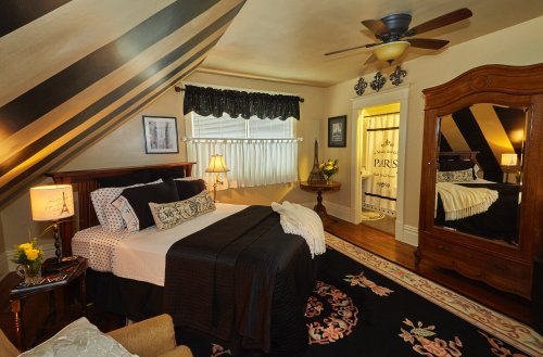 Cozy attic bedroom with striped walls, a wooden bed, and vintage decor, featuring a mirror and floral accents.