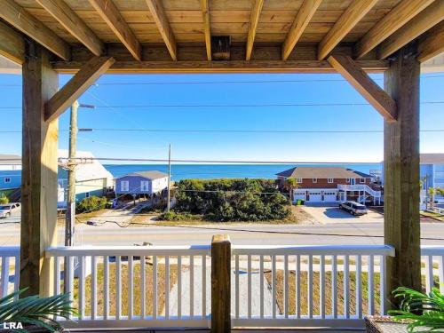 View from a porch overlooking a beach, with houses and greenery in the foreground and a clear blue ocean in the background.