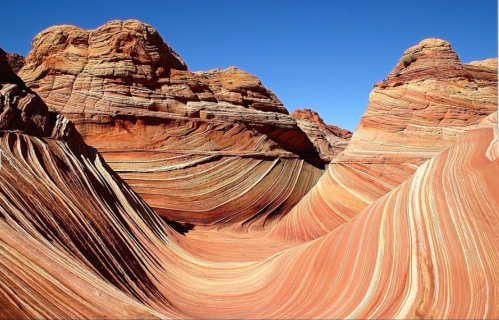 Colorful, wavy rock formations in a desert landscape under a clear blue sky.