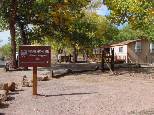 Sign for the Cottonwood Campground Office at the Ksevyone Heritage Area, surrounded by trees and a gravel path.