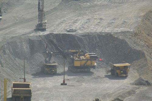 A large mining site with heavy machinery, including trucks and excavators, in a rocky, open area.