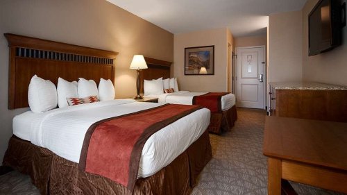 A cozy hotel room featuring two beds, a lamp, and wooden furniture, with warm tones and a welcoming atmosphere.
