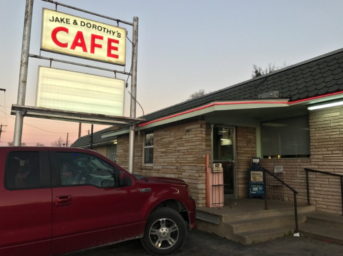 A red truck parked outside Jake & Dorothy's Café, featuring a stone exterior and a lit sign at dusk.