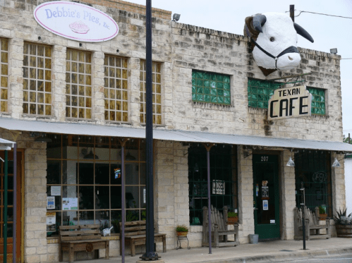 A rustic building featuring a cafe sign and a large cow head mounted above the entrance.