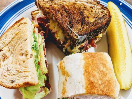 A plate with a toasted sandwich, a wrap, and a pickle, showcasing layers of meat, cheese, and fresh vegetables.
