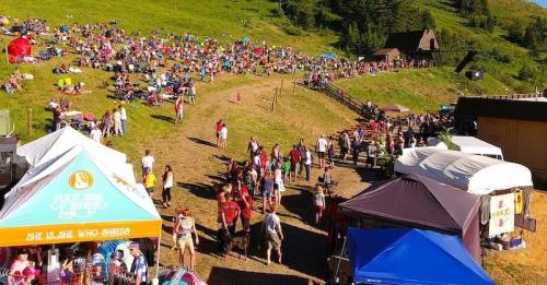A large crowd gathers on a grassy hillside at an outdoor festival, with food stalls and tents in the foreground.