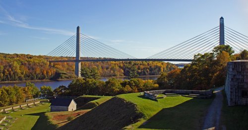 A scenic view of a cable-stayed bridge over a river, surrounded by autumn foliage and historical structures.