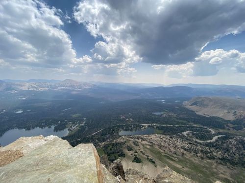 A panoramic view of mountains and lakes under a cloudy sky, showcasing lush greenery and rugged terrain.