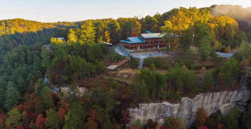 Aerial view of a large wooden building surrounded by colorful autumn trees on a cliffside.