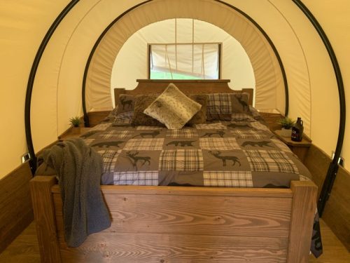 Cozy interior of a glamping tent featuring a wooden bed with patterned bedding and decorative pillows.