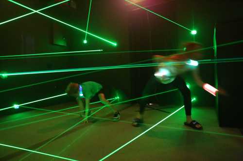 Two children navigate a room filled with green laser beams, using glowing accessories to avoid the lasers.