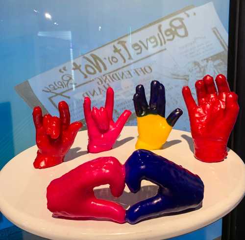 Colorful, painted hands in various poses displayed on a white pedestal against a blue background.