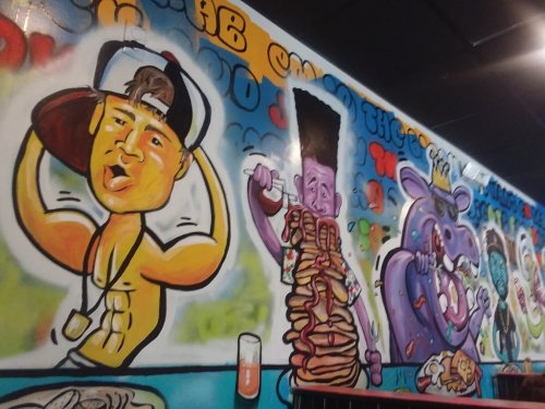 Colorful mural featuring cartoonish characters flexing muscles and enjoying food in a vibrant, playful style.