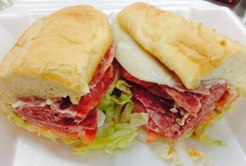 A close-up of a sandwich with layers of deli meats, lettuce, tomato, and cheese in a soft hoagie roll.
