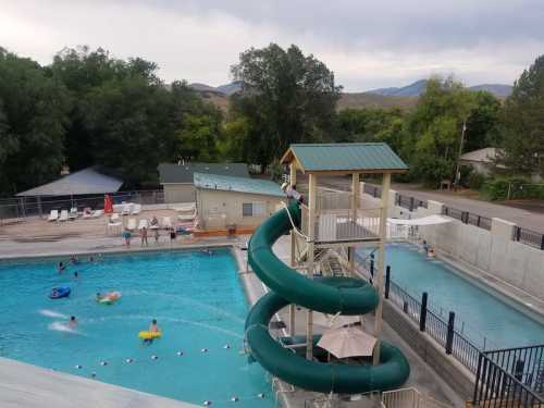 Aerial view of a pool area with a water slide, swimmers, and surrounding trees and mountains in the background.