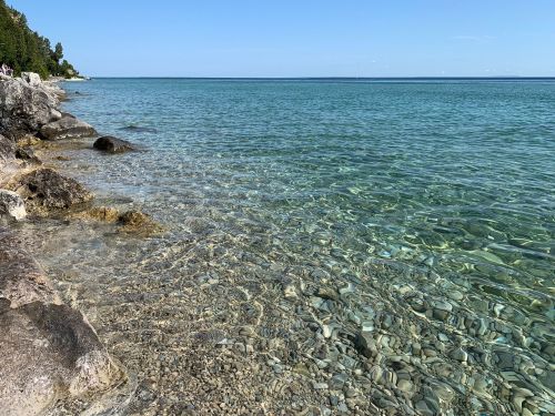 Clear turquoise water gently laps against a rocky shoreline under a blue sky.