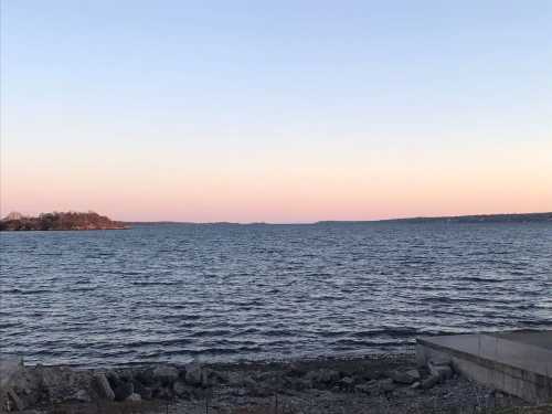 A serene lake at sunset, with gentle waves and a soft pink sky reflecting over the water.