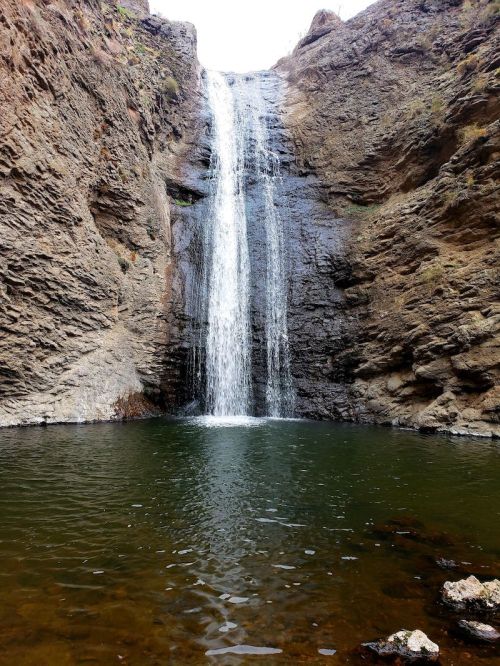 A waterfall cascading down rocky cliffs into a serene pool below, surrounded by rugged terrain.