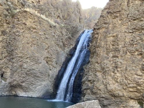 A waterfall cascading down rocky cliffs into a serene pool below, surrounded by rugged terrain.