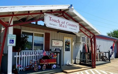Exterior of "Touch of Country Mall," an antique shop with a porch, colorful decorations, and a clear blue sky.