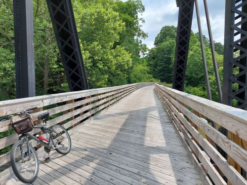 A wooden bridge surrounded by greenery, with a bicycle parked on the side.