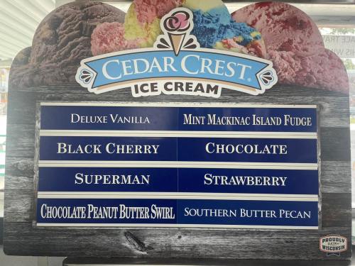 Sign displaying various ice cream flavors: Deluxe Vanilla, Black Cherry, Superman, Mint Mackinac Island Fudge, and more.