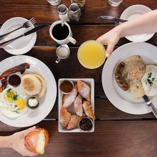 A table set with two breakfast plates, drinks, and a platter of pastries, featuring eggs, bacon, and sauces.