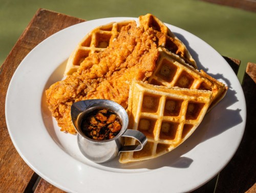 A plate of crispy fried chicken served with golden waffles and a small cup of syrup.