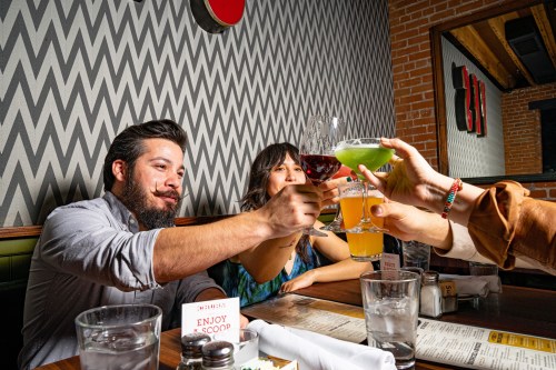A group of friends toasting with drinks at a restaurant, smiling and enjoying their time together.