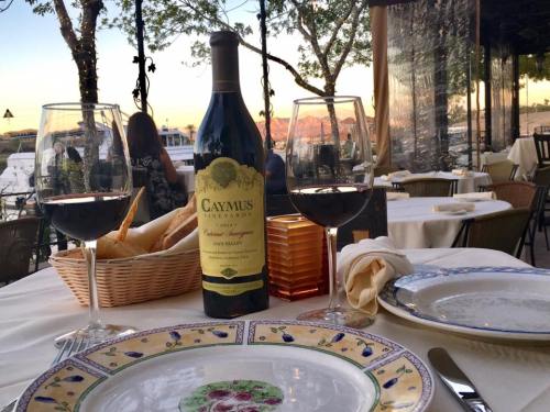 A table set for dinner with a bottle of Caymus wine, two glasses, bread, and a scenic sunset view in the background.