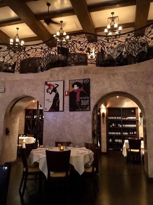 Elegant restaurant interior with arched walls, decorative ironwork, and vintage posters, featuring tables set for dining.